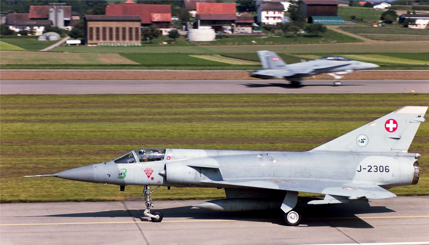 Un velivolo della FlSt 16 in rullaggio per il decollo sulla base di Payerne. Sullo sfondo, il velivolo che ha sostituito i Mirage nella difesa aerea, lo F/A-18 Hornet. Mirage IIIS J-2306 + Hornet