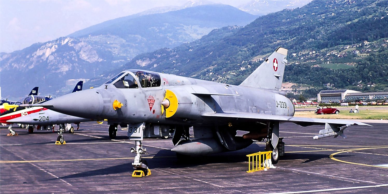 Appeso al pylon alare interno, tra la fusoliera ed il carrello, si intravvede un missile HM-55S. La colorazione giallo ocra dell'ordigno lo identifica come simulacro da esercitazione, privo della testa di guerra e del propulsore. Sul muso del velivolo, il simbolo di una recente campagna d'esercitazione presso la base sarda di Decimomannu. (Sion, Giu. 1989) Mirage IIIS J-2331 a Sion
